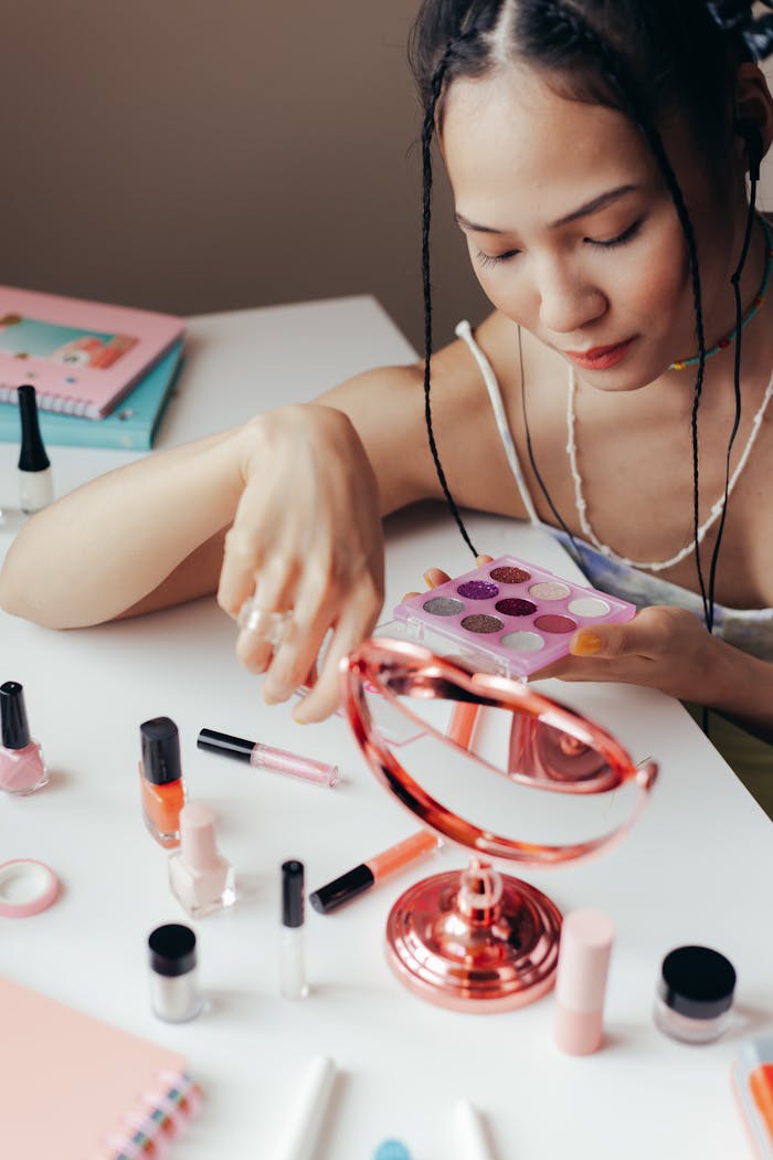 Teen girl experimenting with a vibrant eyeshadow palette, reflecting in a mirror, showcasing colorful makeup artistry.
