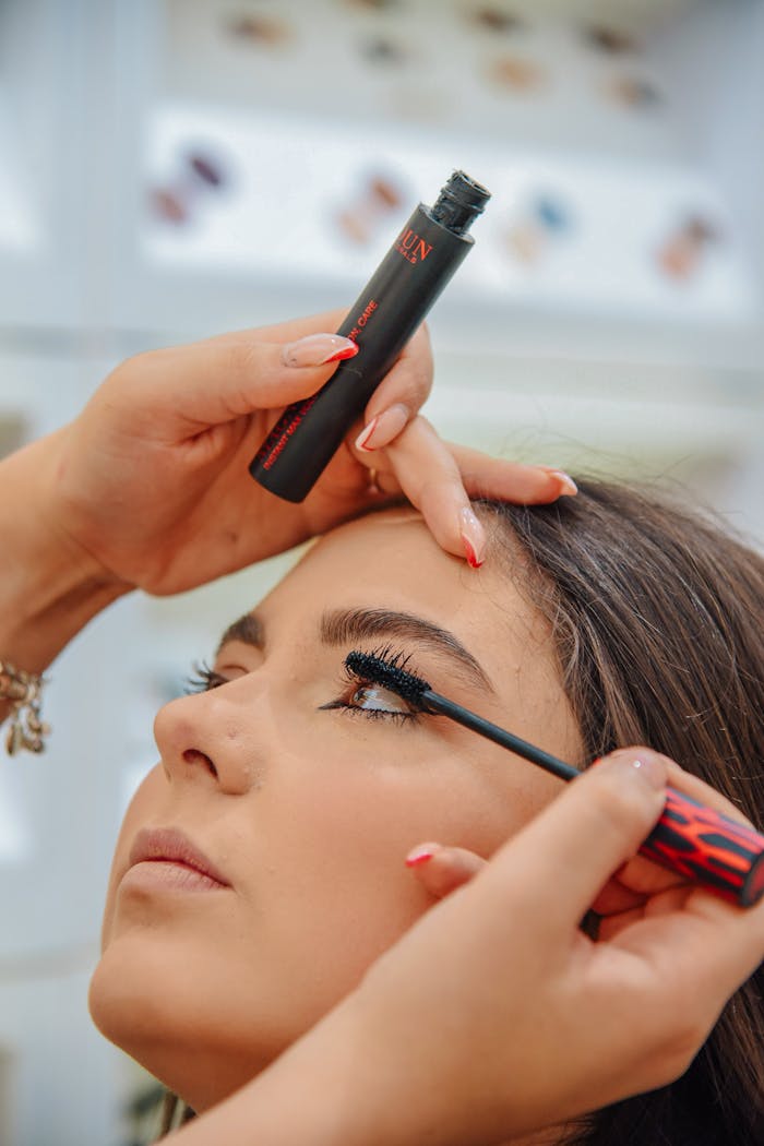 Detailed close-up of a woman applying mascara with focus on eye makeup indoors.