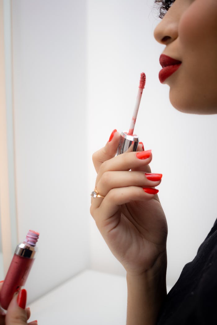 A close-up shot of a woman applying red lip gloss, highlighting beauty and fashion.